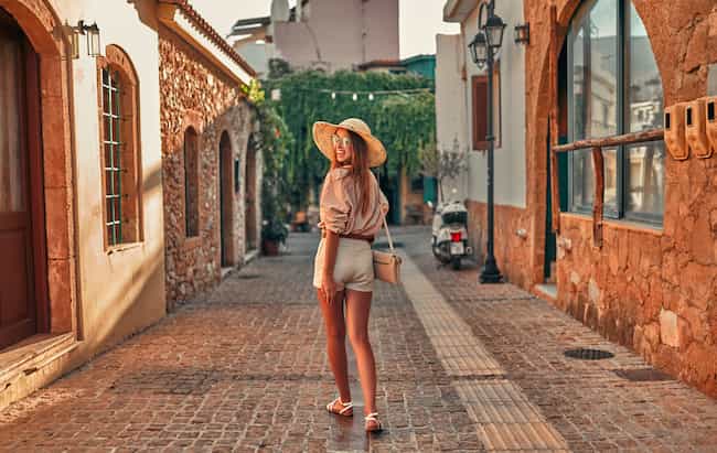 Une touriste séduisante en lunettes de soleil, un chemisier et un chapeau de paille se promène dans les ruelles de la ville. Le concept de tourisme, voyage, loisirs.